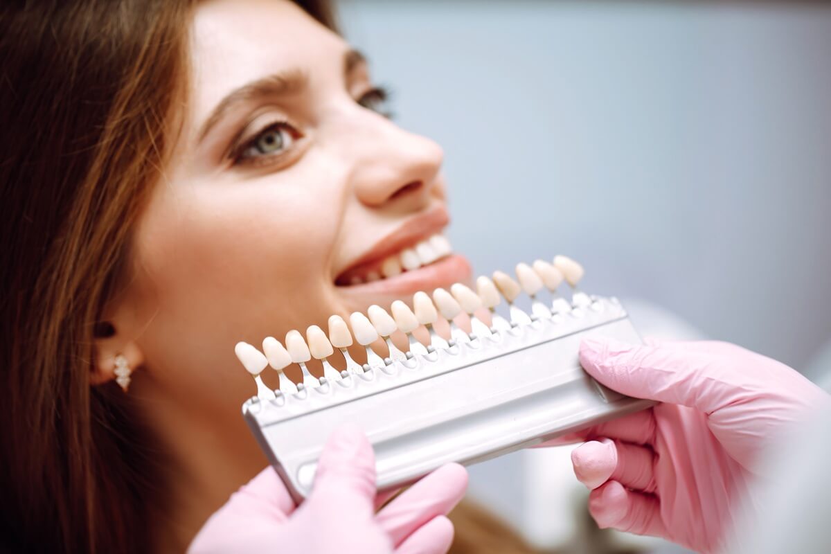 Licówki kompozytowe czy porcelanowe - dentysta dobierający pacjentce kolor licówki