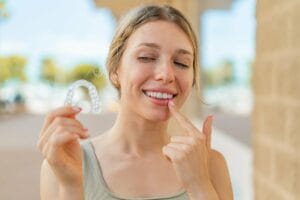 Szyna relaksacyjna na zęby - młoda kobieta trzymająca przezroczystą nakładkę na zęby