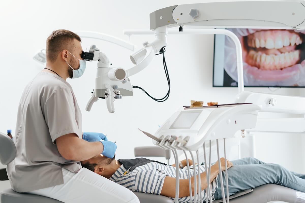 Resekcja wierzchołka korzenia zęba - dentysta przy mikroskopie leczący pacjenta