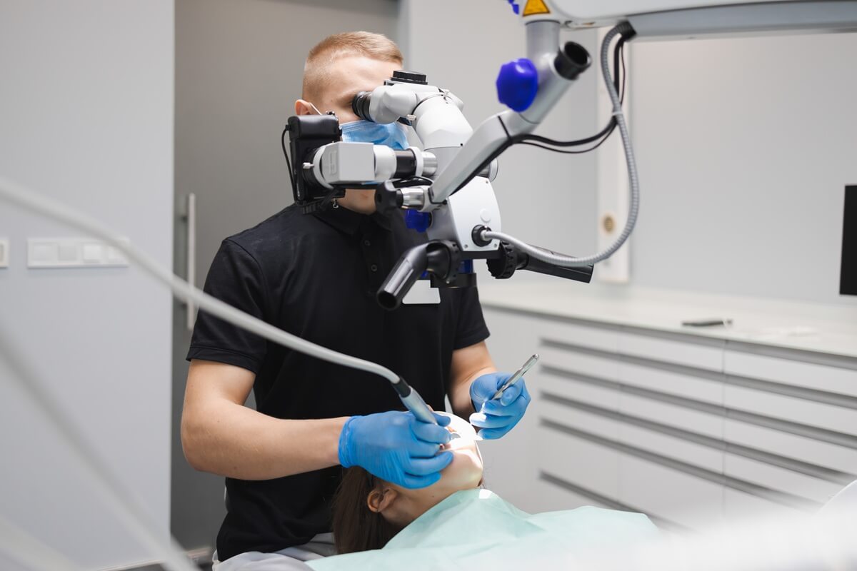 Ból zęba po leczeniu kanałowym - dentysta wykonujący leczenie kanałowe pod mikroskopem u pacjenta